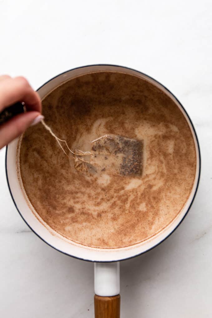 tea bags being dipped in a pot of spices and oat milk