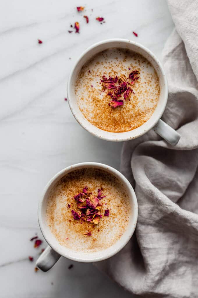 two mugs of chai lattes topped with dried rose petals