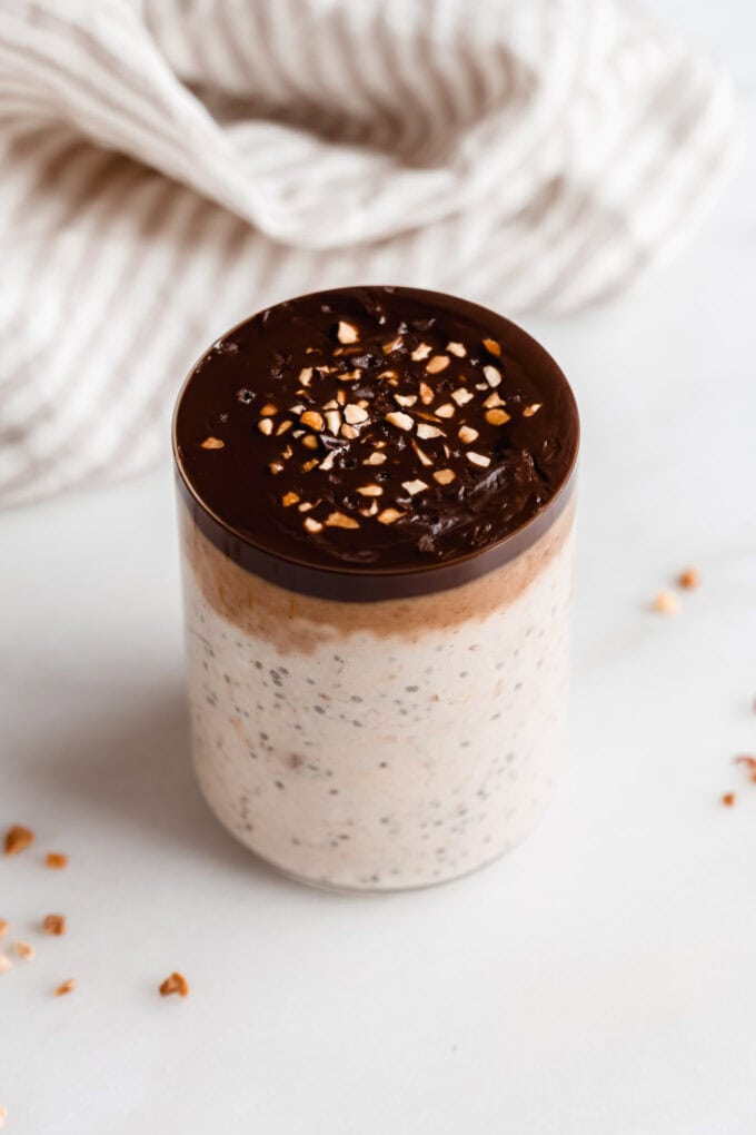 a cup of snickers overnight oats with a beige striped napkin in the back